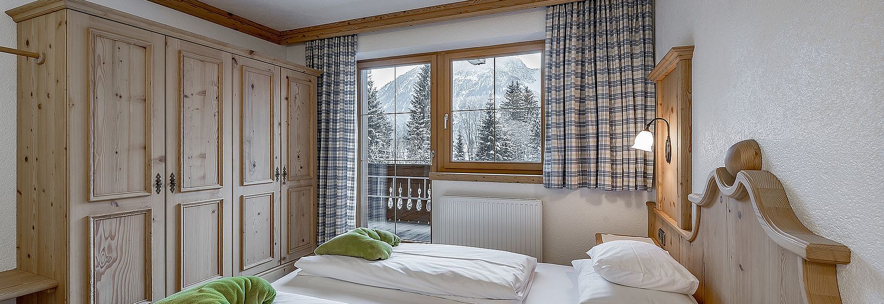 Hotelzimmer mit Doppelbett, Holzmöbeln und Terrasse mit Blick auf die verschneiten Bäume und Berge