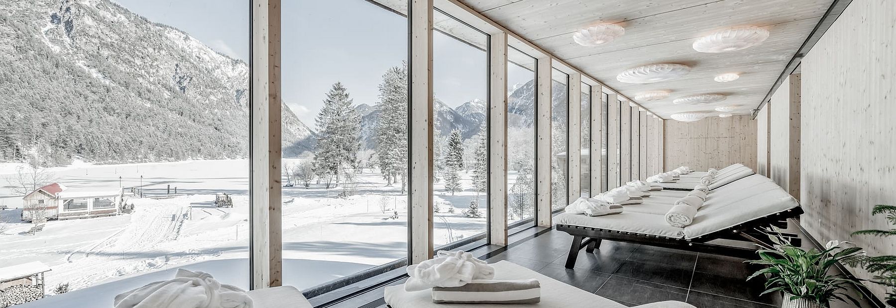 Wellnessliegen mit Kuscheldecke, Badetuch und Bademantel in einem Raum mit großer Glasfassade 