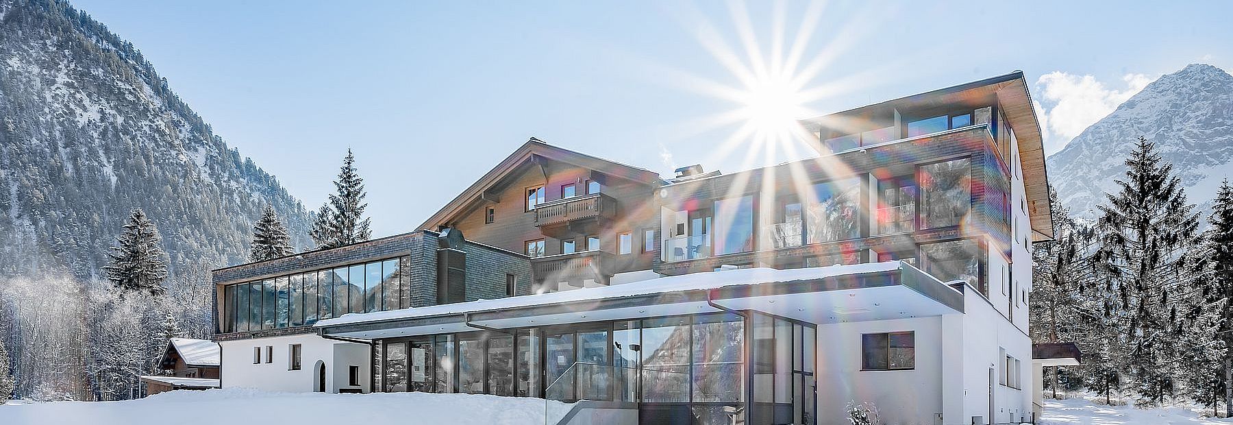 Hotel Fischer am See im Winter bei Sonnenschein mit Blick auf die verschneiten Berge