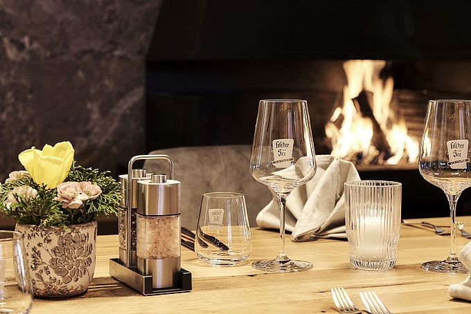 Eleganter gedeckter Tisch mit Weingläsern, Salz- und Pfefferstreuern vor einem Kaminfeuer