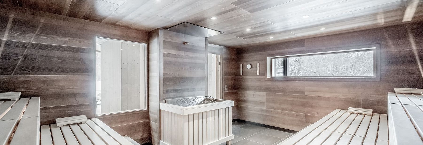 Moderne Sauna mit Liegeflächen, Holzvertäfelung und Blick auf den verschneiten Wald