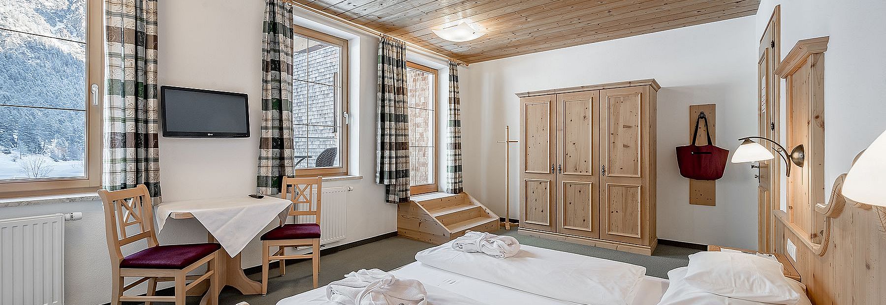 Doppelbett in einem Hotelzimmer mit Holzdecke und Balkon mit Blick auf eine Winterlandschaft