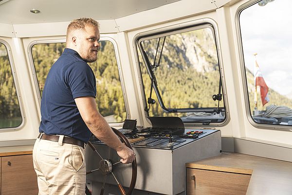 Kapitän am Steuerstand im Inneren des Schiffs mit Blick auf die umliegende Berglandschaft
