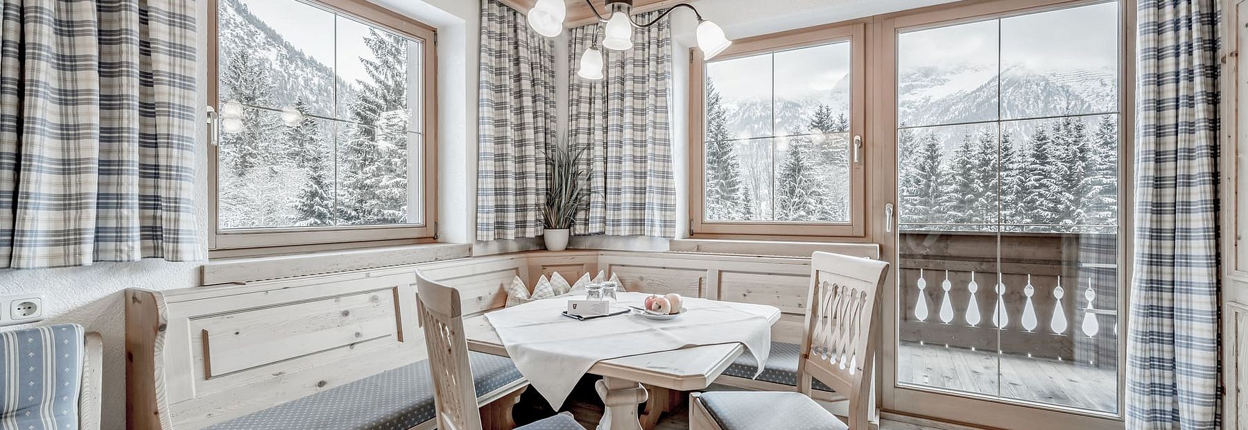 Stube mit Sitzbank und Balkon im Winter mit Blick auf die verschneiten Bäume und Berge