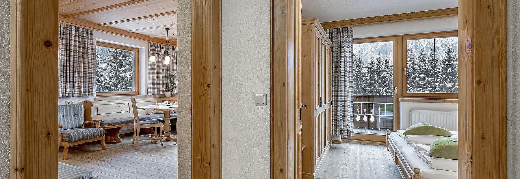 Zimmer mit Stube und Holzmöbeln mit Ausblick auf die verschneiten Bäume und Berge