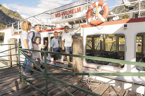 Familie mit Kindern steigt bei sonnigem Wetter lachend auf das Schiff MS Wilhelm am Steg