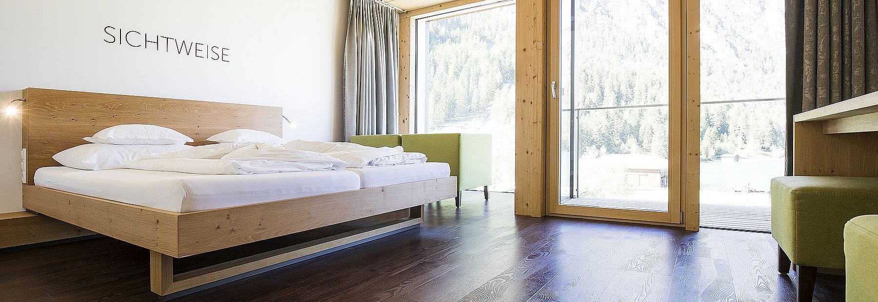 Hotelzimmer mit Doppelbett aus Holz auf Parkettboden und Ausblick auf den Wald im Sommer