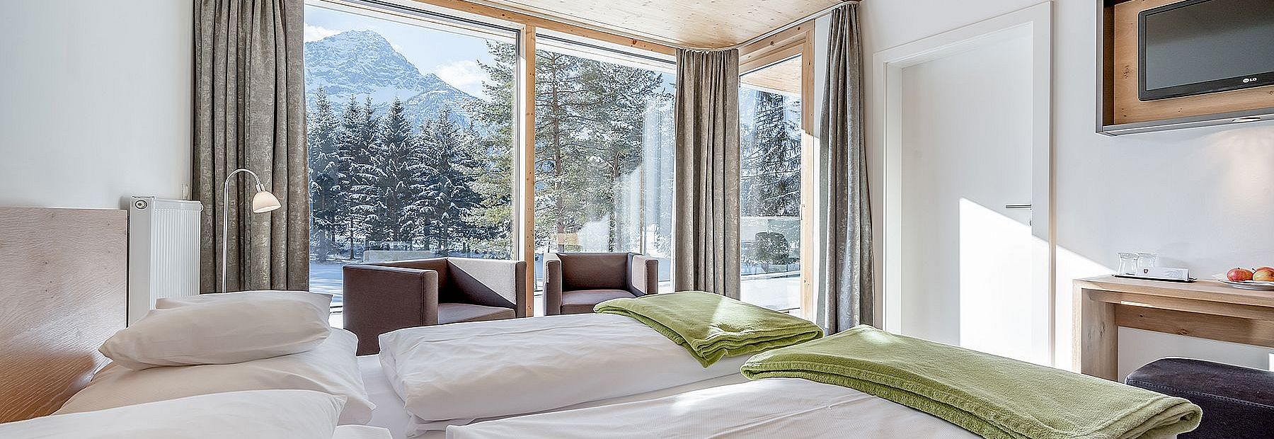 Hotelzimmer mit Doppelbett und Ausblick auf einen verschneiten Wald und die Berge im Winter